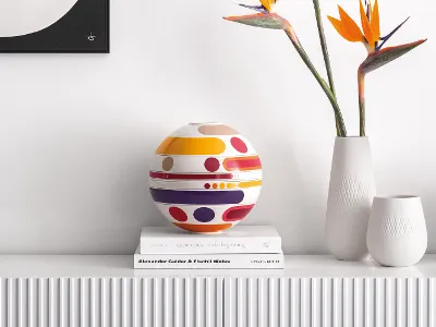 A colorful La Boule Miami on books next to white vases and bird of paradise flowers on a white shelf.