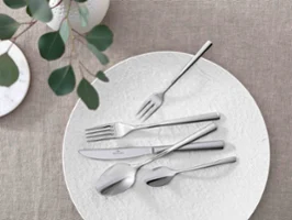 Elegant table decoration with modern Piemont cutlery and decorative greenery on a neutral tablecloth.