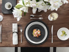 Elegante servicio de mesa con una mariscada en platos Manufacture, flores blancas, una copa de vino blanco y un platito con rodajas de limón.