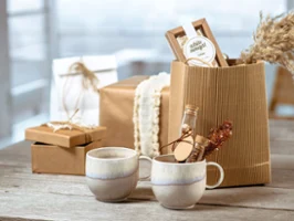 Rustic-look brown gift boxes behind two ceramic mugs from the Villeroy & Boch Perlemor collection on a wooden table.