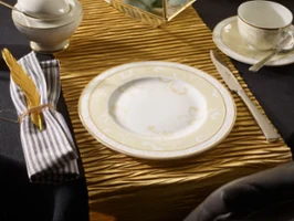 A place setting with plate, knife, fork, cup, saucer and napkin on a table runner with a golden texture.