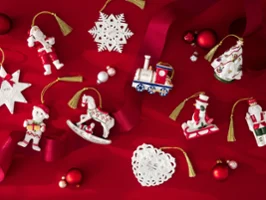Assorted Christmas ornaments including a train, horse, nutcracker, snowflakes, and Santa on a red background with red ribbon and baubles.