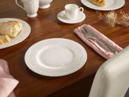 White plate, cutlery on a pink napkin, cup and biscuits on a wooden table set for a meal.