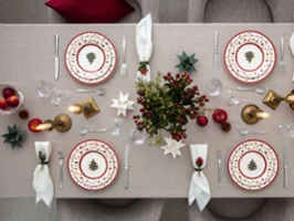 Top-down view of a Christmas-decorated dining table for four people with festive plates, candles, and decorative ornaments.