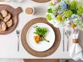 Ein weißer Teller der Kollektion Artesano mit Salat auf einem gedeckten Esstisch. Ein weißer Teller der Kollektion Artesano mit Salat und einer kleinen Quiche, Brot auf einem Artesano Holzbrett und ein Blumenschmuck auf einem gedeckten Esstisch.