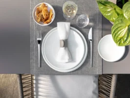 Overhead view of a table setting with white NewMoon plates Overhead view of a table setting with white NewMoon plates, a napkin, cutlery, a cereal bowl, a glass, and a plant on a woven placemat.