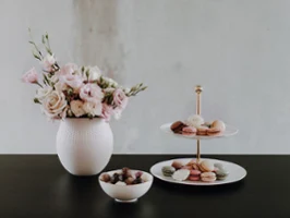 Manufacture vase and MetroChic cake stand A white vase with pink flowers, a multi-tiered tray with desserts and a bowl of chocolates on a dark table.