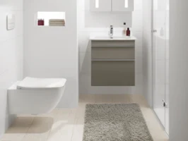 Une salle de bains moderne avec des murs blancs, un lavabo Venticello suspendu avec une armoire de toilette, des WC suspendus et une douche vitrée. Les serviettes et les articles de toilette sont parfaitement rangés sur une étagère en creux. Un tapis beige sur le sol.