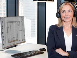 An employee sits at her desk looking at the camera. In the background you can see bathroom planning on the screen