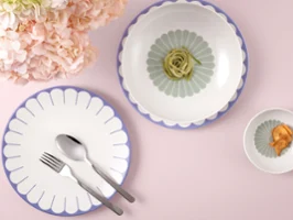 Plate, bowl and dish from the Fleur collection by Villeroy & Boch with food and pink flowers on a light pink background.