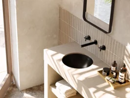 Une salle de bains moderne avec un plan de toilette beige et un lavabo Loop & Friends noir. Parmi les accessoires se trouvent des serviettes et des articles de toilette.