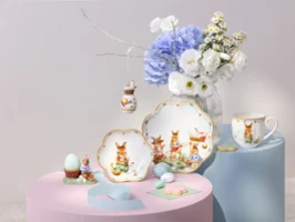 Vaisselle assortie Annual Easter Edition 2026 avec des motifs de lapins, exposée avec des fleurs et des œufs décoratifs sur des supports aux tons pastel.