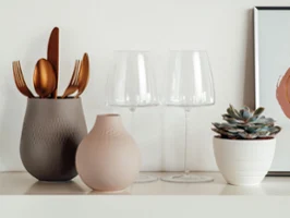 On a shelf, elegant golden cutlery is placed in one of two Manufacture vases, alongside two MetroChic wine glasses.