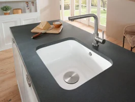 Un lavello sottopiano Cisterna bianco è incassato in un piano di lavoro color antracite. C'è una tavola di legno con sopra un coltello