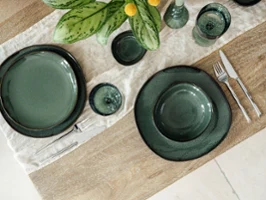 Elegant Table Setting with "Lave Vert" Ceramic Tableware Stylishly set wooden table with "Lave Vert" ceramic tableware, silver "like cutlery" from like. by Villeroy & Boch, and matching Like glasses on a cream-coloured fabric napkin. A green plant with yellow accents complements the elegant arrangement.
