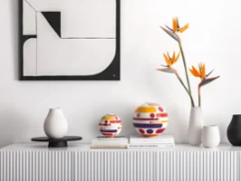 Un buffet minimaliste met en valeur la La Boule Miami moderne, des vases, des fleurs d'oiseau de paradis et des livres empilés sous une œuvre d'art murale abstraite.