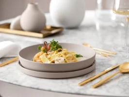 A plate of pasta with shrimp, garnished with herbs, on an elegant dining table with golden flatware and a glass of white wine.