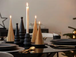 A black table, laid with black plates, gold cutlery and candle decorations in the shape of trees and pine cones.