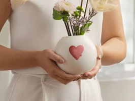 Okrągły wazon marki with love z czerwonym motywem serca Kobieta trzymająca okrągły biały wazon marki with love z czerwono-różowym sercem i białymi kwiatami.