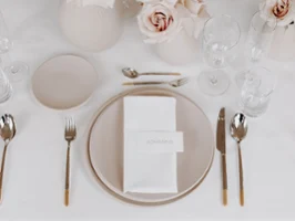 A table at a wedding reception set with NewMoon dinnerware and glasses A festively set table with white and beige NewMoon plates, Ella flatware and NewMoon glasses.