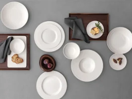 A formal table setting with a white bowls and plates on a grey table and food on it.