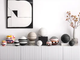 Une série de La Boule sphériques, colorées, rayées et à motifs, est posée sur une console blanche sous une œuvre d'art abstrait et un vase de fleurs orange.