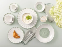 Table setting with Villeroy & Boch Fleur Vert plates, croissant, yogurt, coffee, and white flowers on a light green background.