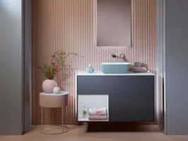 Meuble sous plan Finion bleu foncé de Villeroy & Boch dans une salle de bains rose avec une table basse rose.