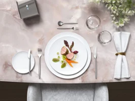 Stylish marble table with gourmet food on white MetroChic plates, together with MetroChic cutlery and floral decorations.