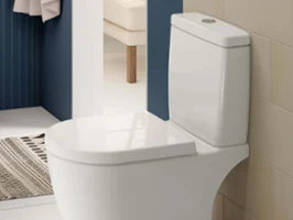 Des WC sur pied blanc avec un réservoir de chasse d’eau dans une salle de bains nette aux murs beige et bleu