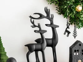 Two black Black Xmas reindeer on a black console table below a hanging green wreath with black ornaments.