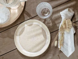 Beige Perlemor plate on a wooden table A beige Perlemor plate and a napkin on a wooden table.