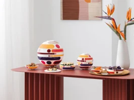 A modern interior with La Boule and La Petite Boule, a white Manufacture Collier blanc vase with orange flowers, and abstract wall art in muted tones.