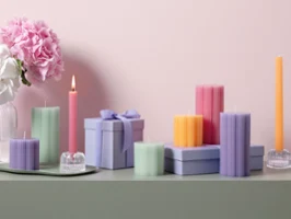 Fleur candles in various pastel colors and shapes as the ideal gift idea Various pastel-colored candles from Fleur and decorative gift boxes on a green surface with pink and white flowers in the background.