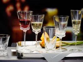 A selection of Villeroy & Boch Grand Royal crystal glasses, each containing a different drink, artfully arranged on a silver tray next to a folded napkin and an orange tulip.