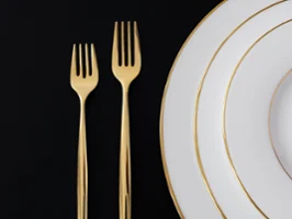 Golden forks from the MetroChic collection and plates from the Anmut collection by Villeroy & Boch on a black background.
