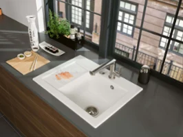 A modern kitchen sink with sushi on a plate, with a view of the city through large windows.