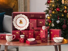 A table with an advent calendar and festive tableware from Villeroy & Boch next to a decorated Christmas tree in a cozy living room.