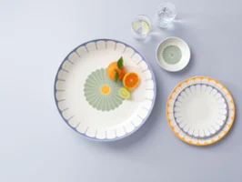 A large plate with orange slices and a mint leaf, next to two smaller plates and two glasses of water, on a light grey surface.