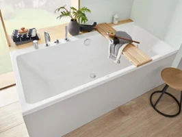 Baignoire blanche avec tablette en bois, plante, serviette et tabouret à proximité dans une salle de bains moderne avec lumière naturelle.