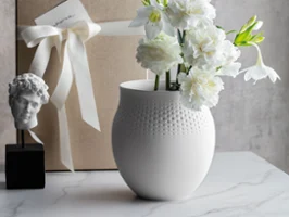Manufacture Collier Blanc Big Perle Vase Duży wazon Manufacture Collier Blanc Perle z delikatną fakturą w kropki, z zapakowanym prezentem w tle, przeznaczony do obfitych kompozycji kwiatowych.