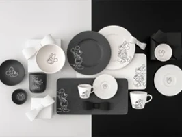 Toute la collection Manufacture Mickey avec des assiettes, tasses et bols noirs et blancs sur un fond noir et blanc divisé.
