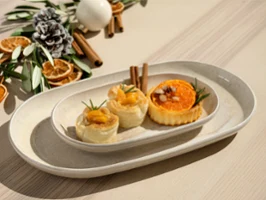 Three assorted pastries on a Perlemor white oval plate, with dried orange slices and cinnamon sticks in the background.