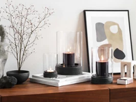 A modern home interior with a wooden sideboard and a dried flower with three Manufacture hurricane lamps.