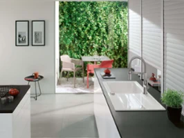 An Architectura ceramic sink with kitchen tap on a black worktop with a group of tables in the background