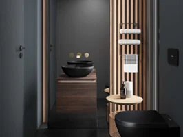 Une salle de bains moderne avec des murs sombres, un plafond en lamelles de bois et diverses touches décoratives. Elle dispose de WC noirs Loop & Friends de Villeroy & Boch, d’une vasque à poser, d’un grand miroir, d’une lampe suspendue et d’une petite table avec des articles de toilette.