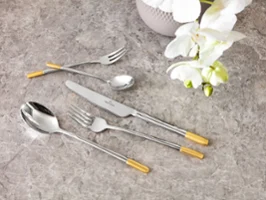 Elegant Ella-bestikksett med gylne detaljer på en marmorbordplate, ledsaget av en hvit orkidé.