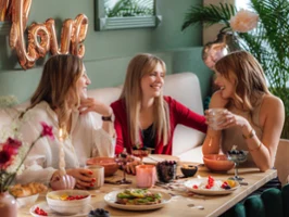 A festive scene with three women at a table with Perlemor dinnerware and Like glass from like. by Villeroy & Boch, and balloons in the background.
