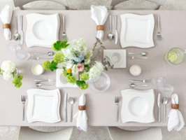 Top-down view of a minimalist table setting featuring NewWave porcelain plates, coffee cup and saucer, Boston and Boston Green glassware, and both NewWave and Blacksmith cutlery. Flower vases adds a natural and elegant touch to the clean composition.