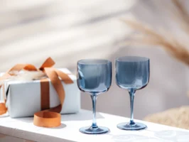 Blue Like glasses in front of a gift box Two Villeroy & Boch Like Glass wine glasses in blue on a white table next to a wrapped gift with a brown bow.